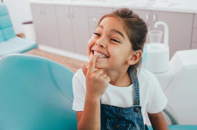 A happy child pointing to her teeth in a dental chair.