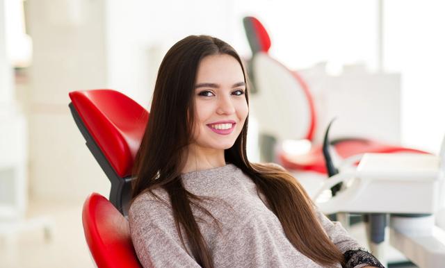 a woman is sitting in a red dental chair and smiling .