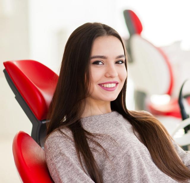 a woman is sitting in a red dental chair and smiling .