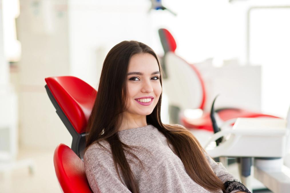 a woman is sitting in a red dental chair and smiling .