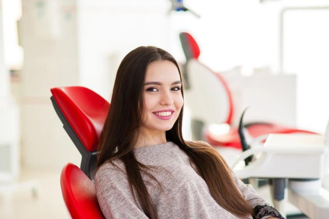 a woman is sitting in a red dental chair and smiling .