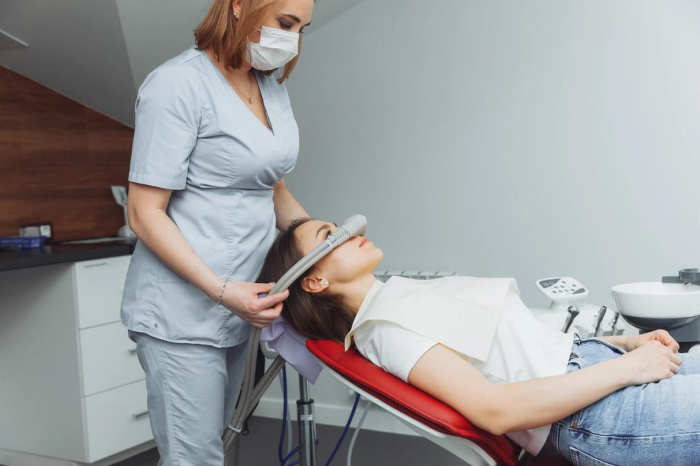 a woman is laying in a dental chair while a nurse holds a machine to her face .