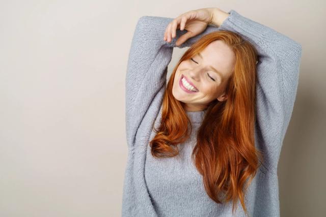 a woman with red hair is wearing a grey sweater and smiling with her eyes closed .