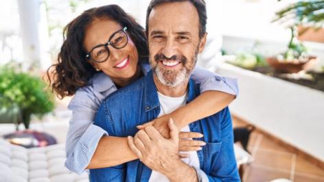 A smiling woman hugs a smiling man from behind.