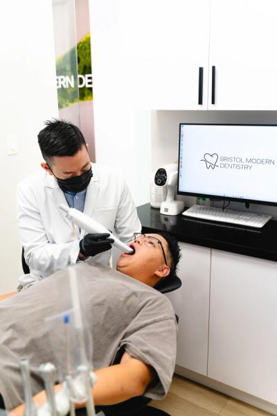 A dentist uses an intraoral scanner on a patient's open mouth.