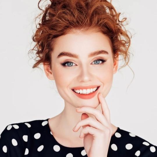 a woman with red hair is smiling and touching her face with her hand .