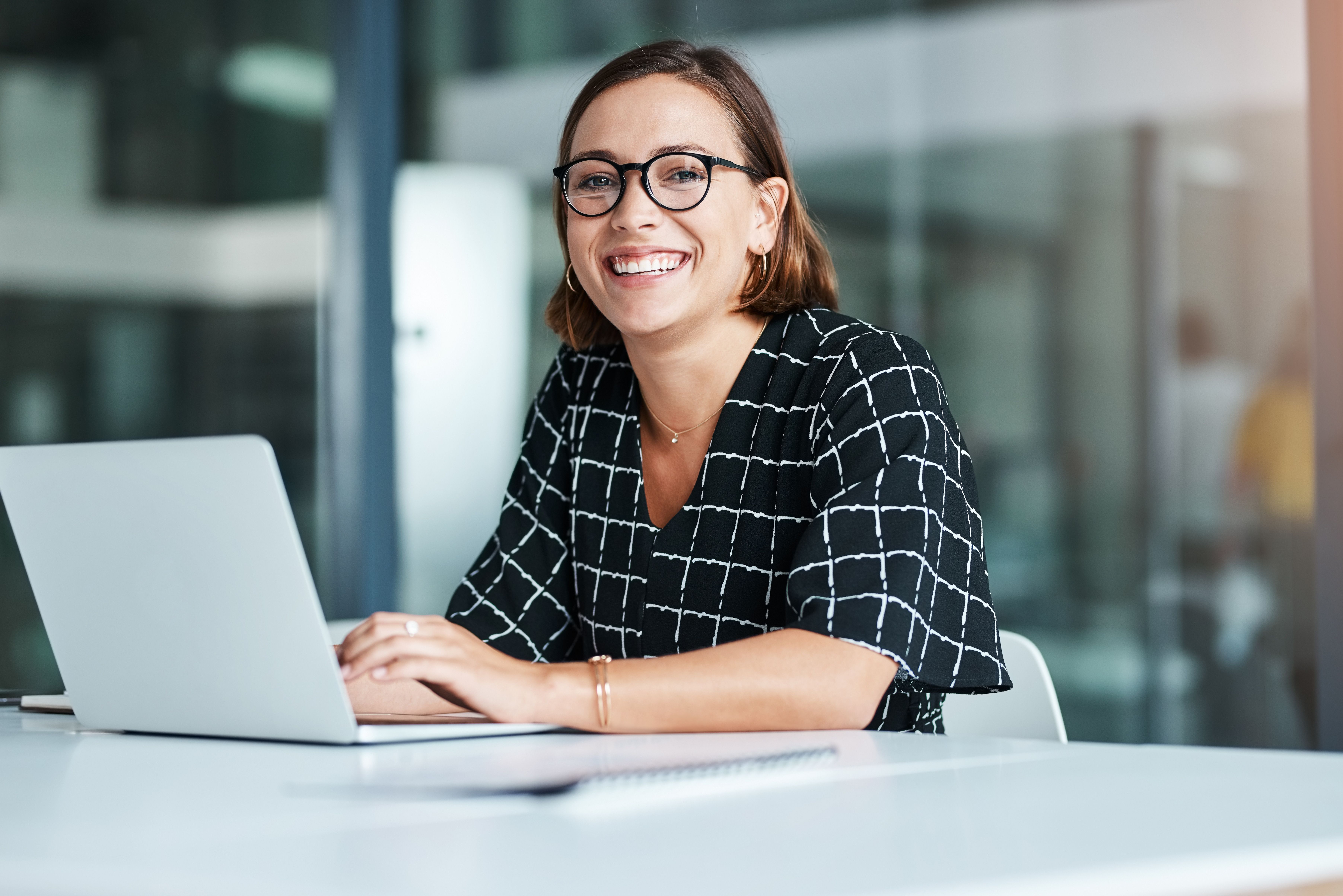 a woman is sitting at a table with a laptop computer and smiling .