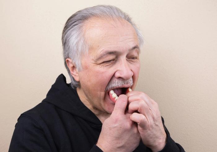 an elderly man is holding a tooth in his mouth .
