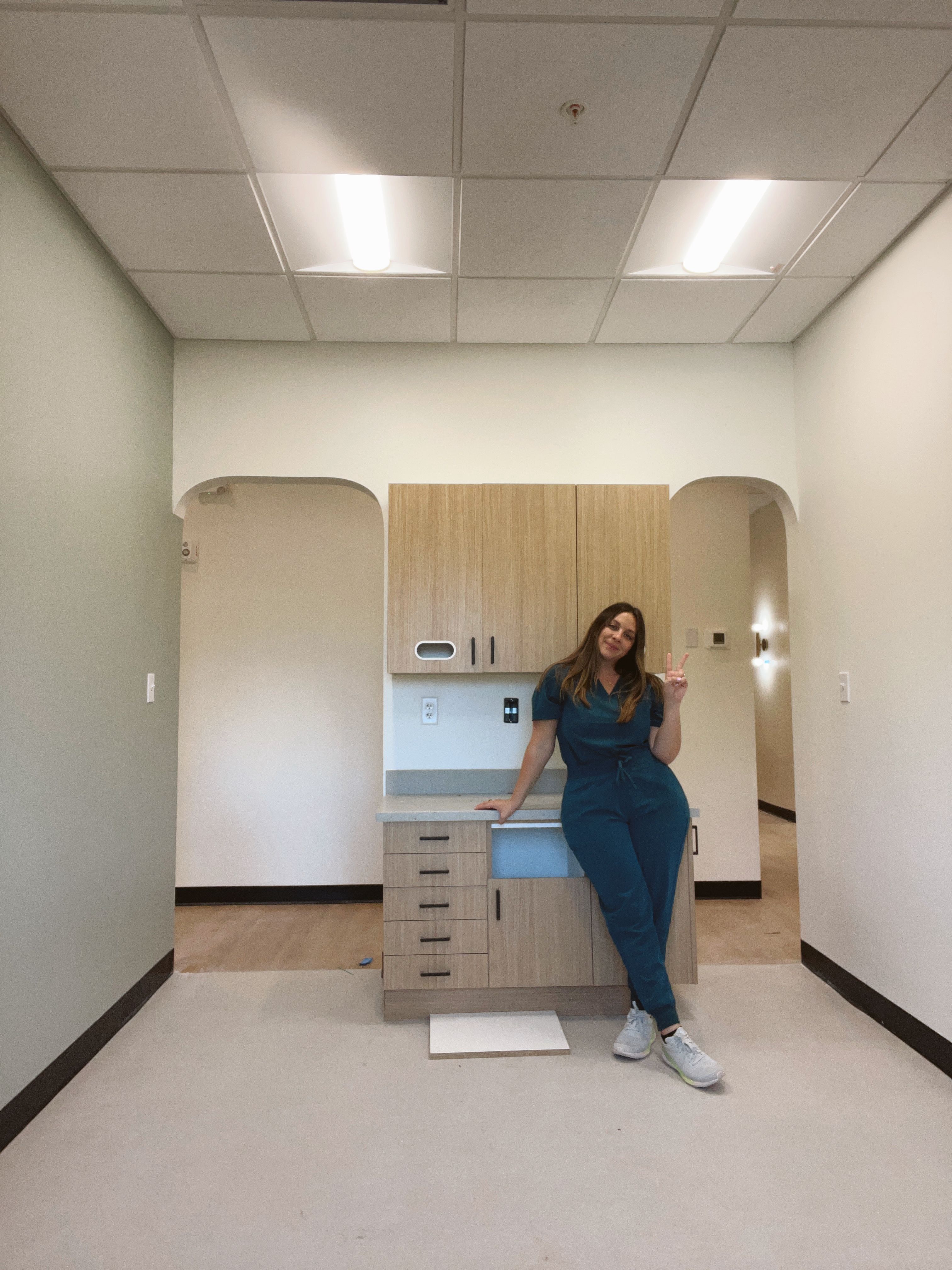a woman in scrubs sits on a counter in an empty room