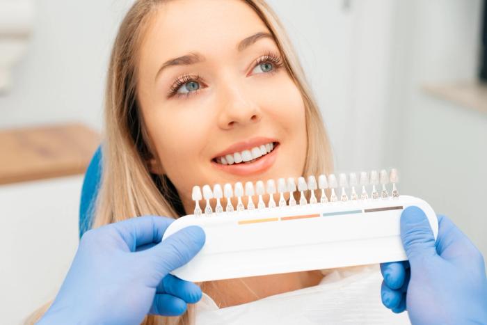 a woman is sitting in a dental chair while a dentist is holding a tooth color chart .