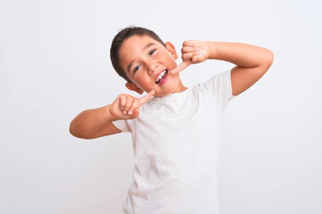 A smiling boy pulls the corners of his mouth to show his teeth.