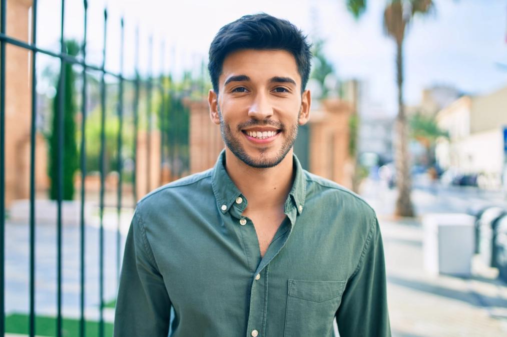 A smiling young man in a green shirt stands outdoors.