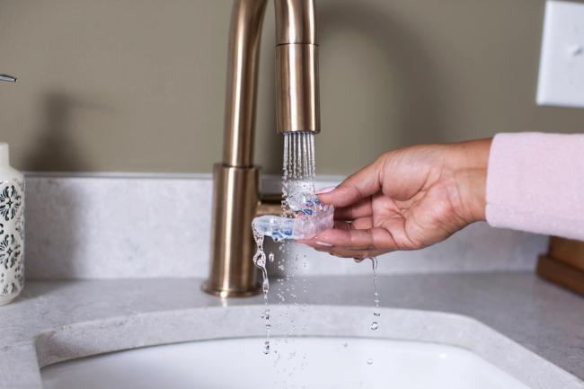 a person is washing a mouth guard in a bathroom sink .