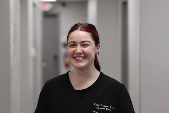 a woman in a black scrub top is smiling in a hallway .
