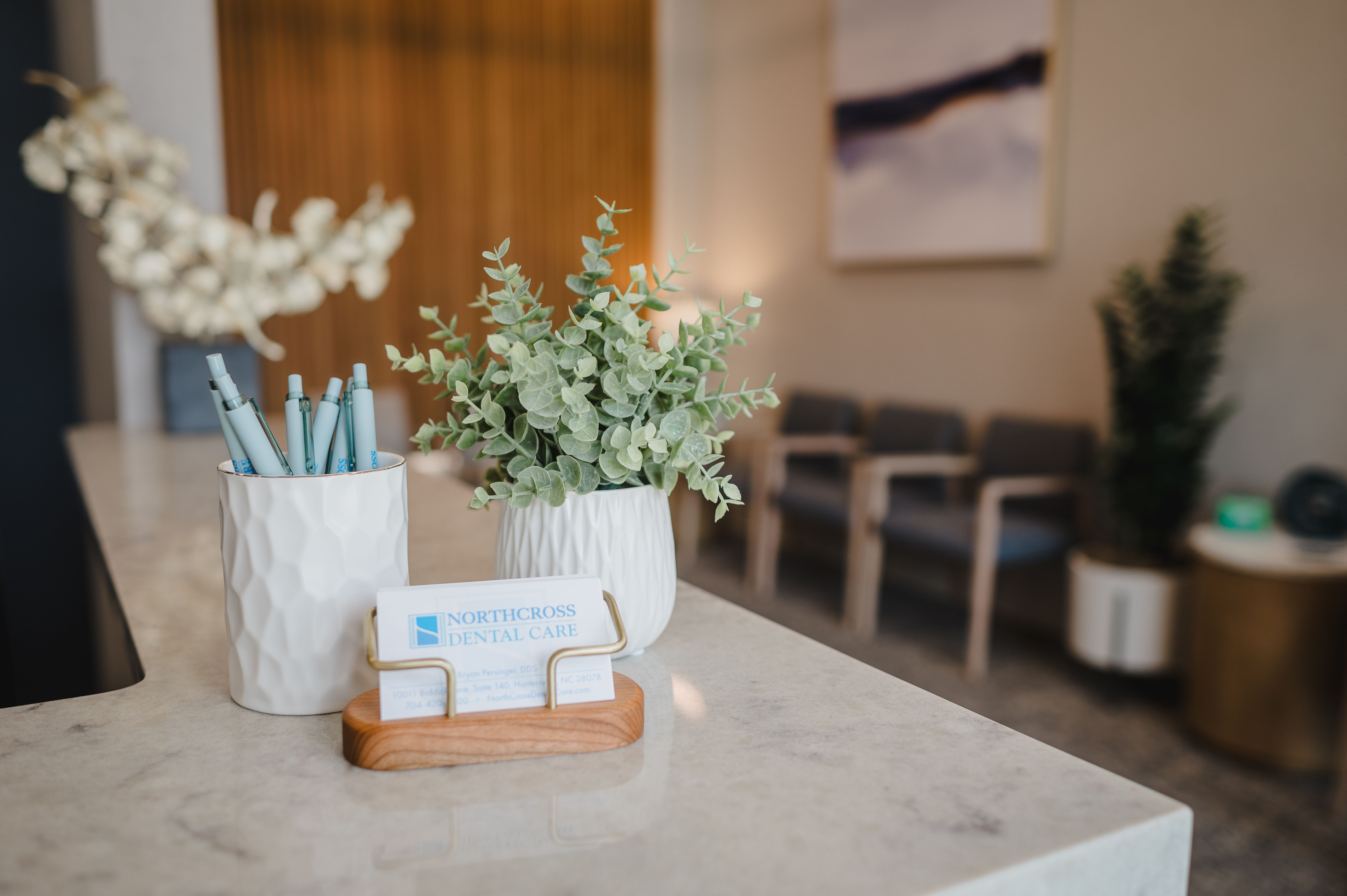a dental office with a plant , pens , and a business card on the counter .