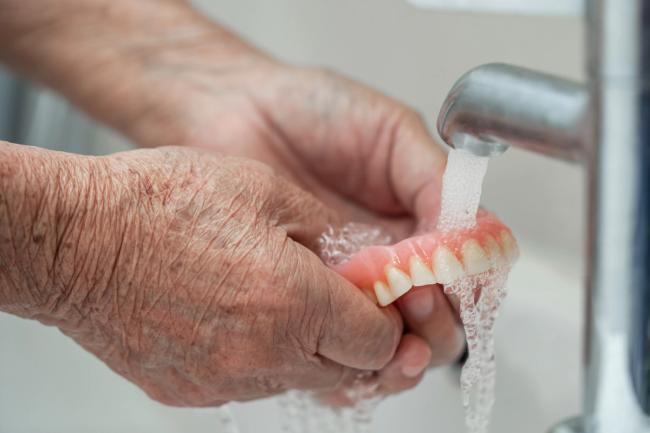 an elderly woman is washing her dentures in a sink .