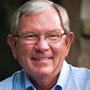 a man wearing glasses and a blue shirt is smiling for the camera .