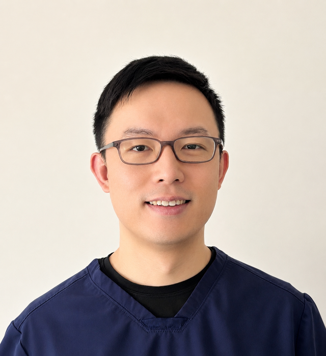 A smiling man wearing glasses and a blue scrub top.
