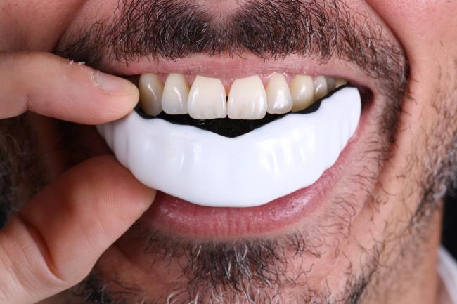 a man with a beard is putting a mouth guard on his teeth .