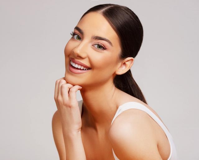 a beautiful young woman is smiling with her hand on her chin .