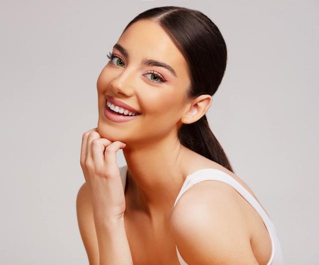a beautiful young woman is smiling with her hand on her chin .