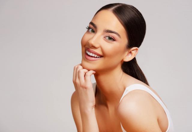 a beautiful young woman is smiling with her hand on her chin .