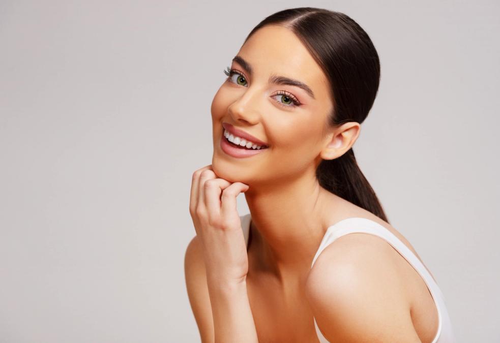 a beautiful young woman is smiling with her hand on her chin .