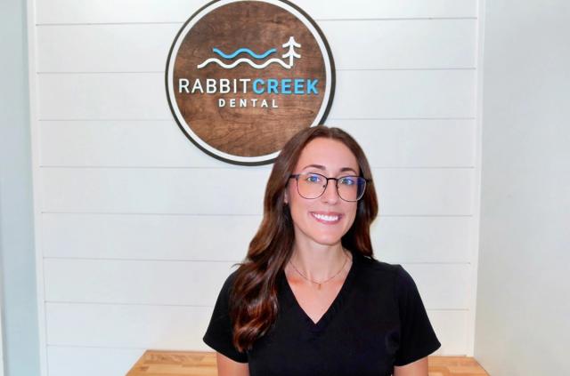 a woman wearing glasses is smiling in front of a rabbit creek dental sign .