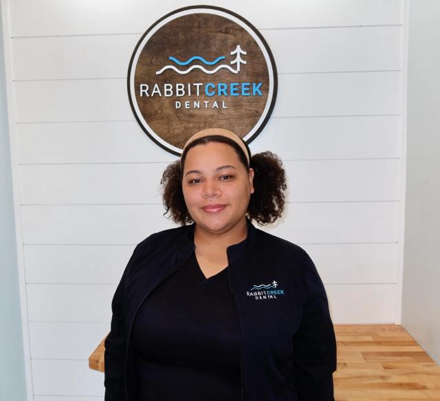 a woman is standing in front of a rabbit creek dental sign .