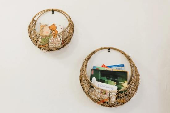 Two round, woven baskets hang on a white wall, one holding stuffed animals and the other holding books.