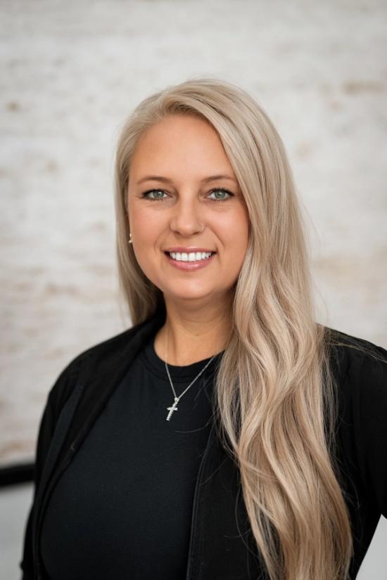 a woman with long blonde hair is wearing a black jacket and a cross necklace .