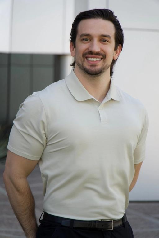 a man wearing a white polo shirt and black pants smiles for the camera