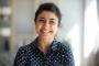 A smiling young Indian woman in a blue polka dot shirt.