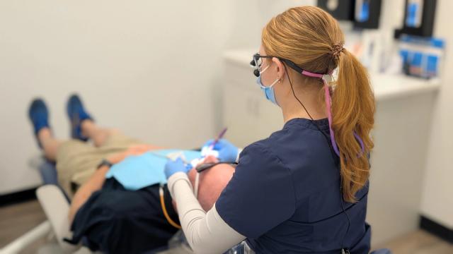 a female dentist is examining a man 's teeth in a dental office .