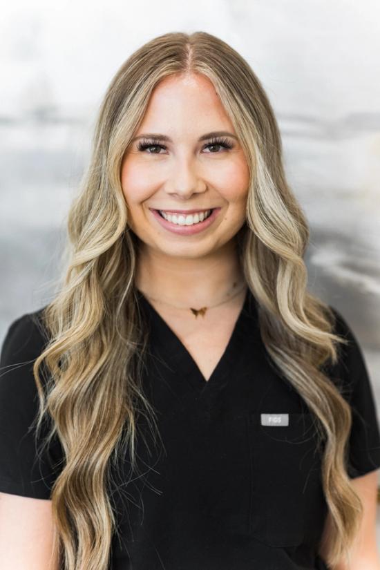 the woman is wearing a black scrub top and smiling for the camera .