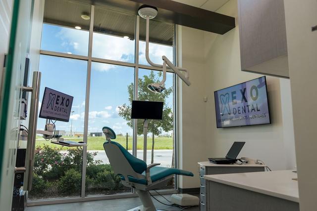 a dental office with a dental chair , desk , monitor and television .