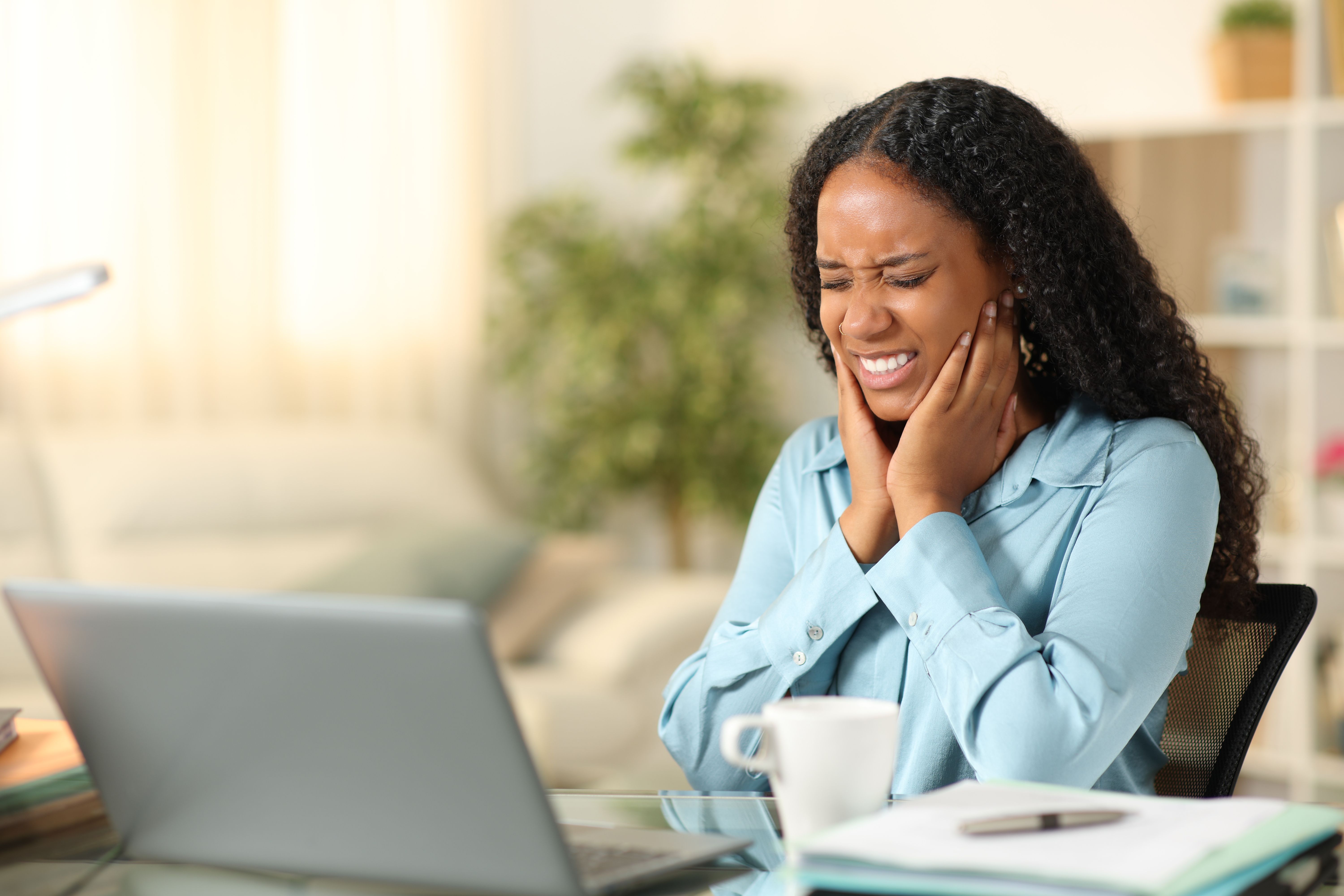 a woman is sitting at a desk with a laptop and holding her ear .