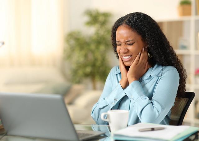 a woman is sitting at a desk with a laptop and holding her ear .