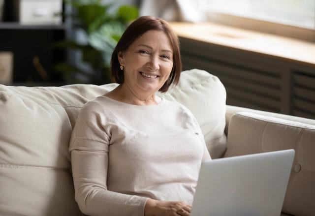 an elderly woman is sitting on a couch using a laptop computer .