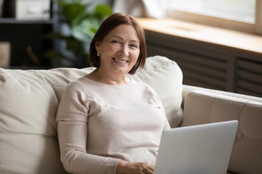 an elderly woman is sitting on a couch using a laptop computer .