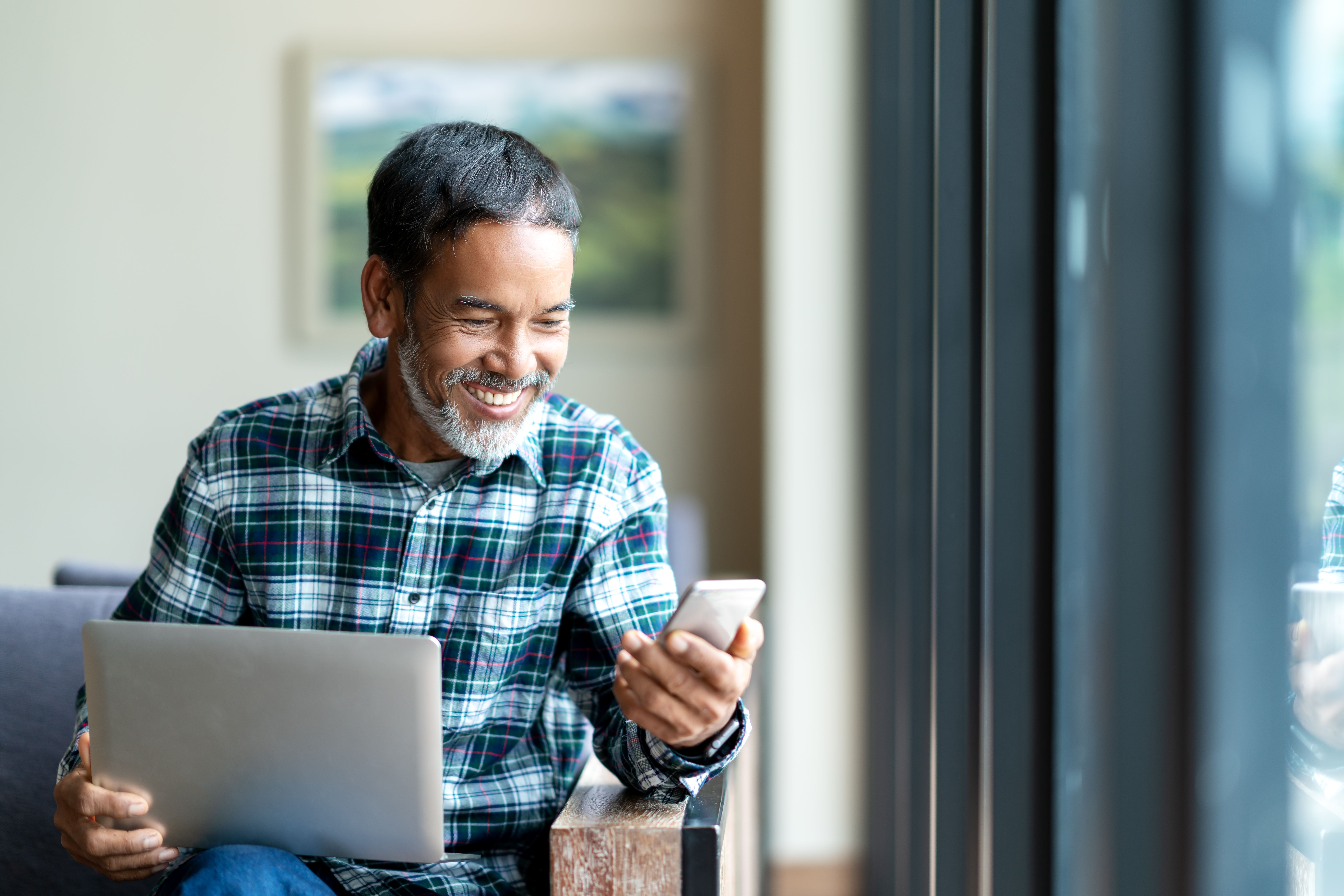 a man is sitting in a chair using a laptop and a cell phone .