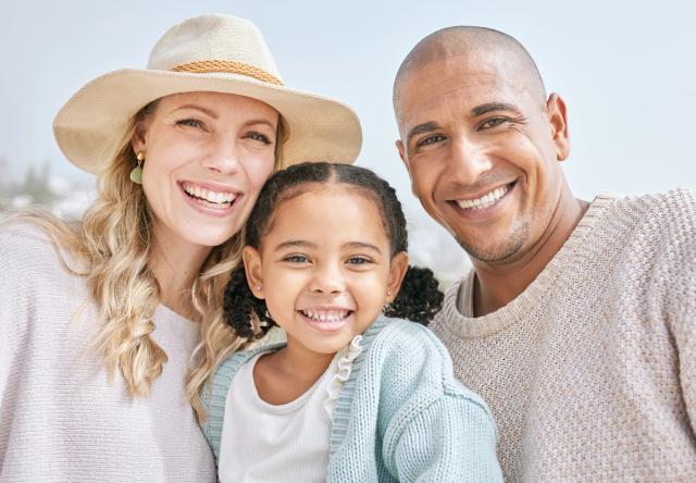 a family is posing for a picture on the beach and smiling for the camera .