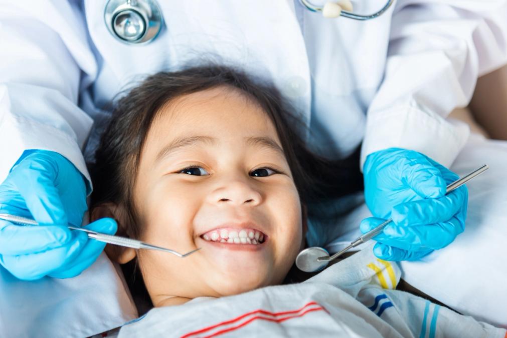 A smiling child at the dentist, with gloved hands holding dental tools.