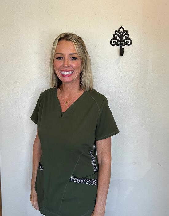 a woman in a green scrub top is smiling in front of a white wall .