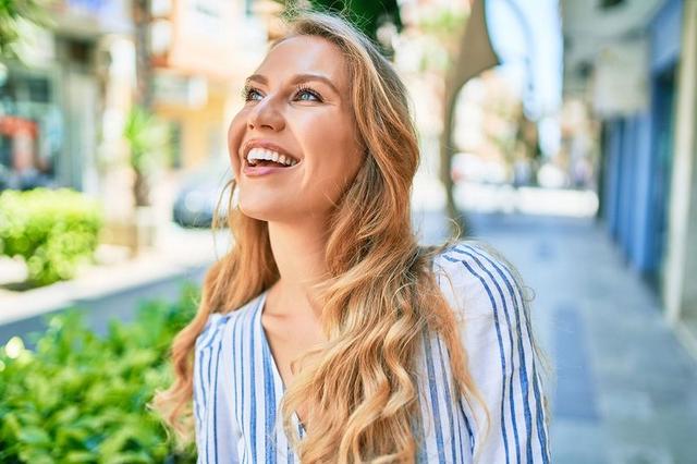 a young blonde woman is smiling and looking up at the sky while walking down the street .