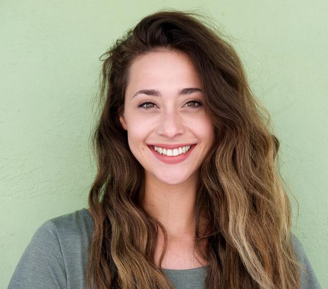 a woman with long hair is smiling in front of a green wall .