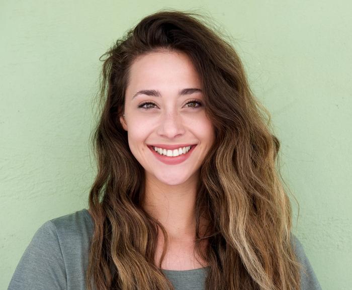 a woman with long hair is smiling in front of a green wall .
