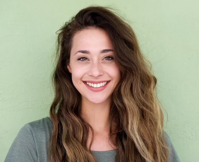a woman with long hair is smiling in front of a green wall .