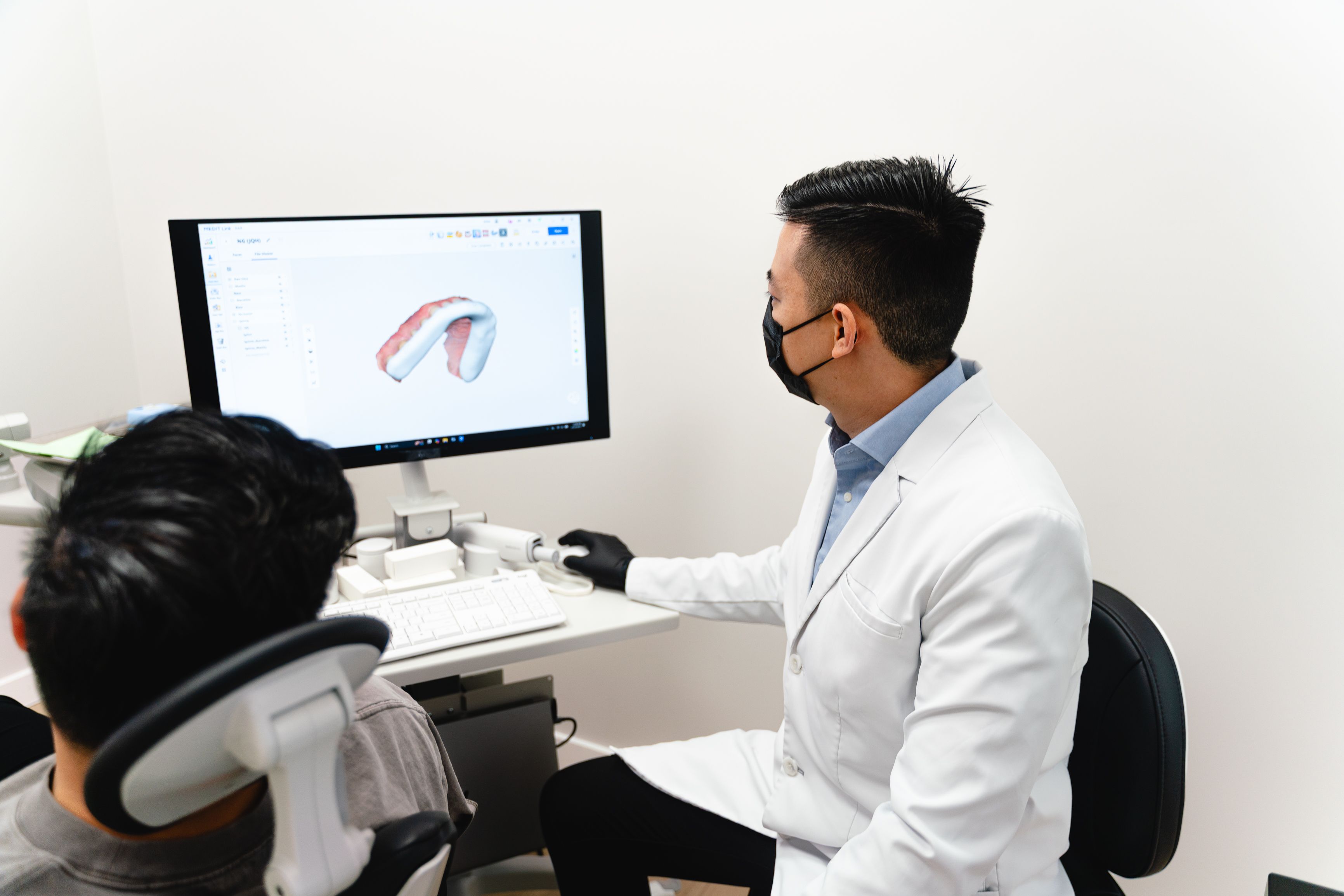 A dentist shows a patient a 3D dental model on a computer screen.
