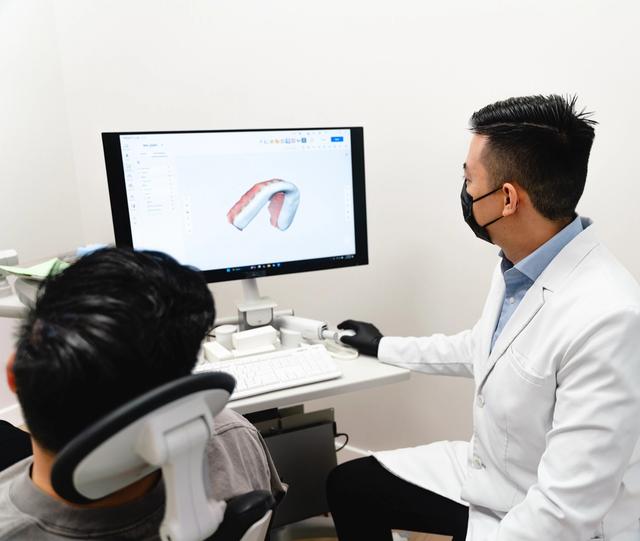 A dentist and patient look at a 3D digital dental model on a monitor.